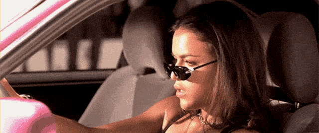 a woman wearing sunglasses is sitting in a pink car .