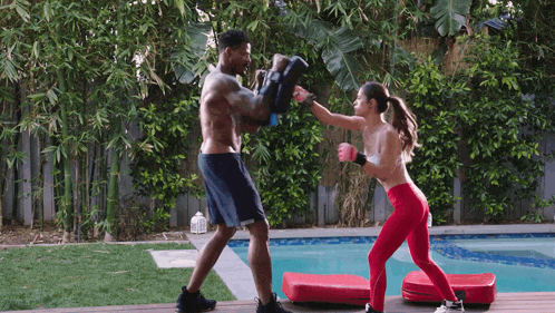 a man and a woman are boxing in front of a swimming pool