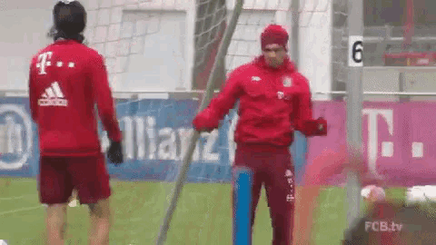 a man in a red adidas jacket stands next to another man on a field