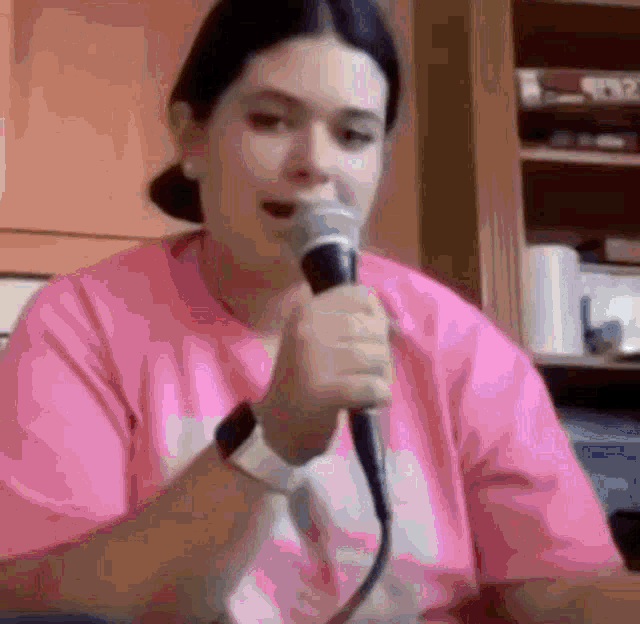 a woman in a pink shirt is holding a microphone in her hand .