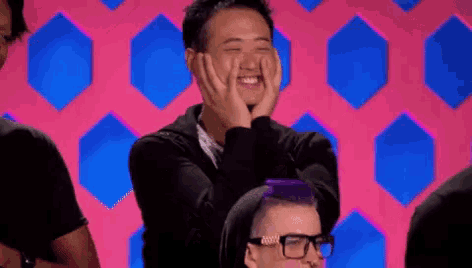 a man with purple hair is covering his face with his hands and smiling