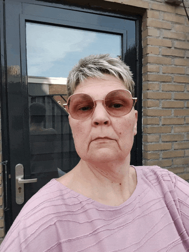 a woman wearing sunglasses stands in front of a black door