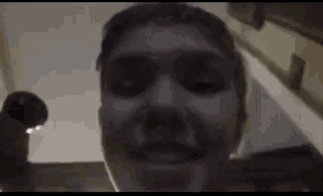 a close up of a man 's face in a dark room with a staircase in the background .
