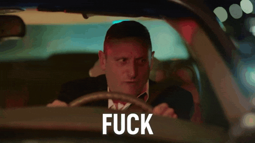 a man in a suit and tie is driving a car and the word fuck is on the side