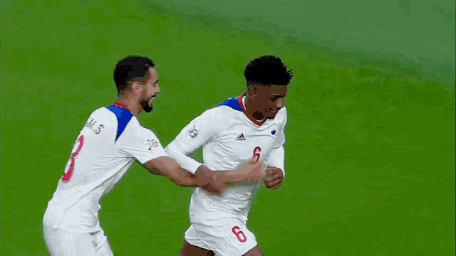two soccer players one with the number 6 on his shorts are running on the field