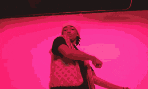 a man in a white hat is standing in front of a pink background and making a funny face .