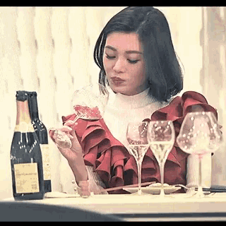 a woman is sitting at a table with a bottle of wine and glasses of wine .