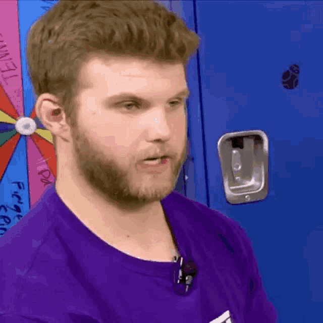 a man in a purple shirt is standing in front of a blue locker with a spinning wheel on it