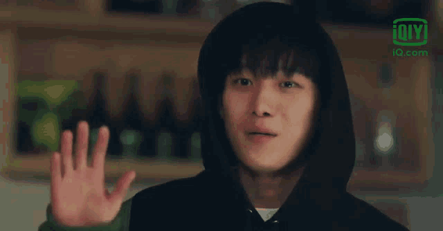 a young man wearing a black hoodie is waving his hand in front of a sign that says iq.com