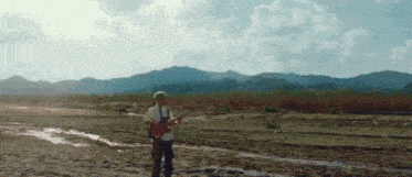 a man playing a guitar in a muddy field