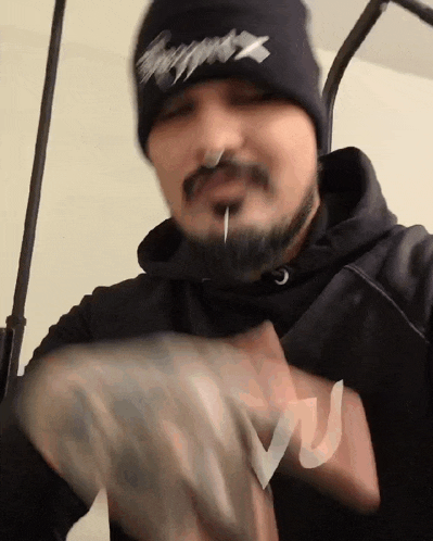 a man with a beard wearing a black beanie with the letter x on it is holding a bag of money