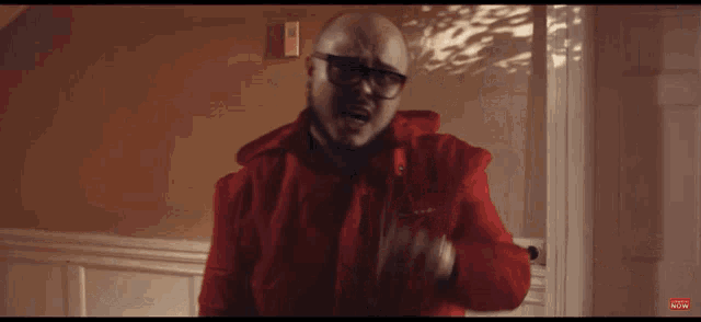 a man wearing glasses and a red jacket is pointing at something