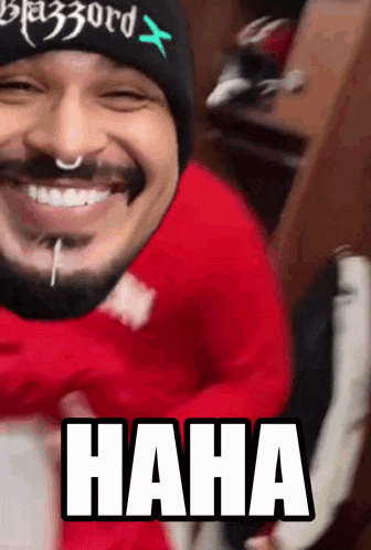 a man with a beard wearing a beanie and a red shirt is laughing with the word haha written below him
