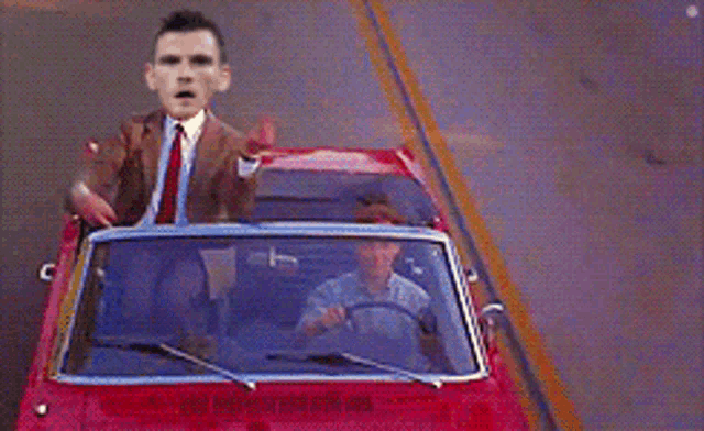 a man in a suit and tie is driving a convertible car