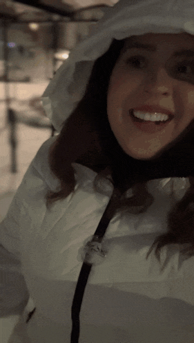 a woman in a white jacket with a hood smiles