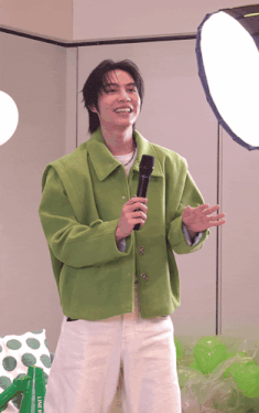 a man in a green jacket is holding a microphone in front of a light