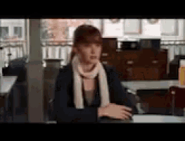 a woman wearing a scarf is sitting at a table in a room .