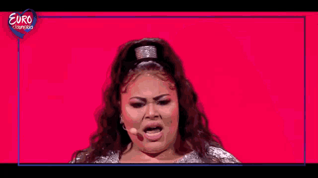 a woman with long hair and a silver dress is making a funny face on a red background .