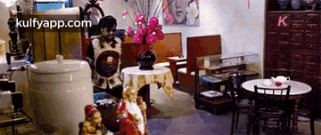 a room with tables and chairs and a vase of pink flowers