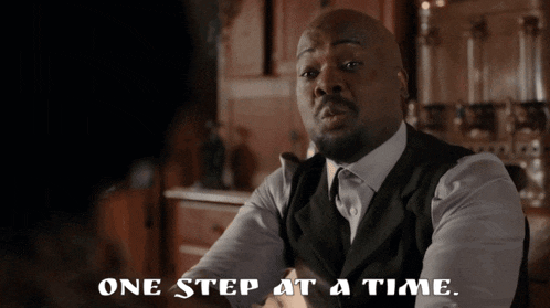 a man in a suit and tie is sitting in front of a sign that says one step at a time