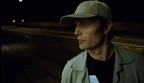 a man wearing a baseball cap and a green jacket looks to the side at night