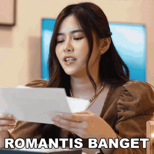 a woman holding a piece of paper with the words romantis banget on the bottom