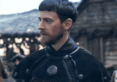 a man with a beard is wearing a black cape with a silver emblem on the chest