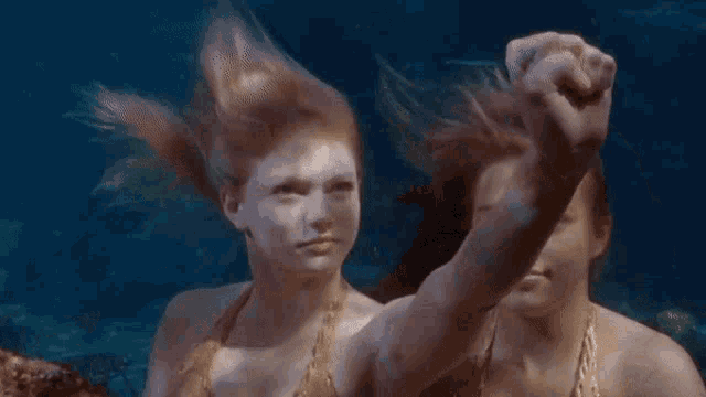 two mermaids are swimming in the ocean and one is blowing a kiss