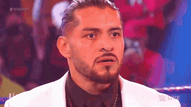 a man with a beard is wearing a white suit and a black shirt and is looking at the camera .