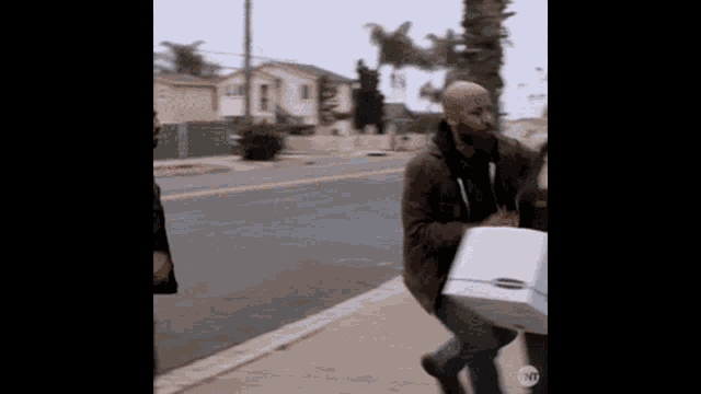 a man with a tattoo on his face is walking down the sidewalk carrying a box