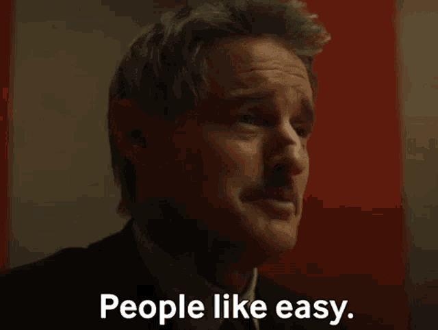 a man in a suit and tie is talking to another man and saying `` people like easy '' .