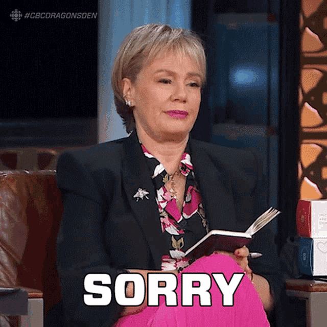 a woman is sitting in a chair holding a book and making a sorry sign .