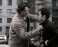 two men are standing next to each other on a city street . one of the men is adjusting the other 's tie .