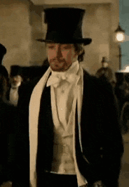 a man in a tuxedo and top hat is walking in a crowd .