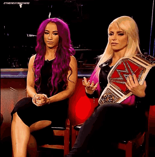 a woman with purple hair is sitting next to a woman with blonde hair holding a championship belt