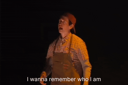 a man in a plaid shirt and apron is giving a thumbs up while standing in the dark .