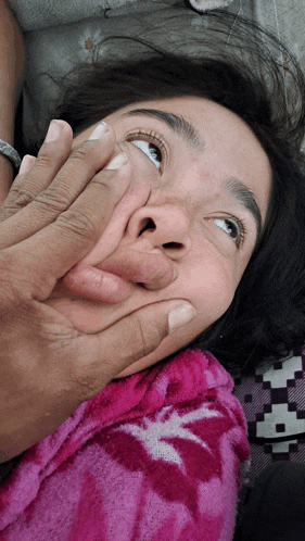 a person covering a woman 's mouth with a pink blanket