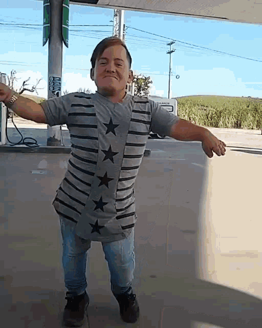 a man wearing a striped shirt with stars on it is standing in front of a gas pump