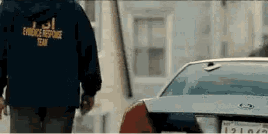 a man in a evidence response team jacket is walking towards a car .