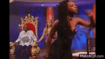 a woman is dancing in front of a man who is sitting in a chair