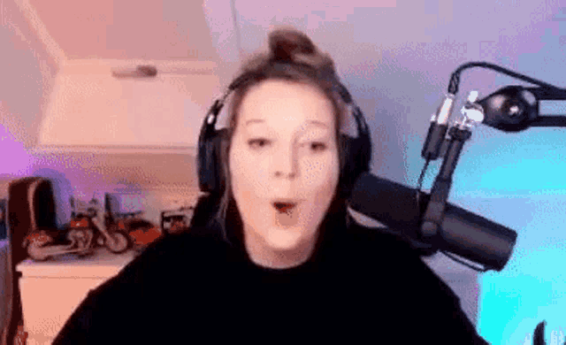 a woman wearing headphones is standing in front of a microphone and making a funny face .