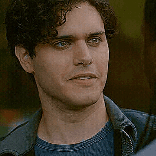 a man with curly hair and blue eyes is wearing a blue shirt and a jacket .