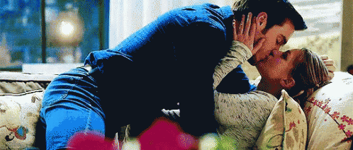 a man and woman are kissing on a couch in a living room .