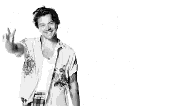 harry styles is wearing a white shirt and plaid pants and giving a peace sign .