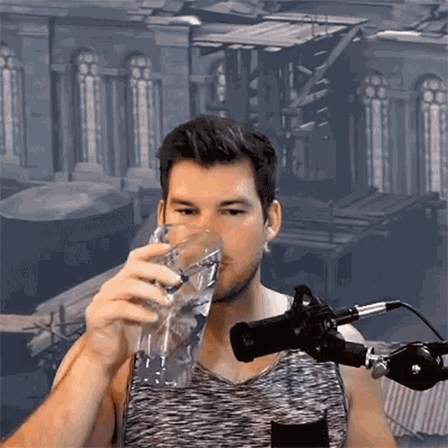 a man is drinking from a glass while standing in front of a microphone