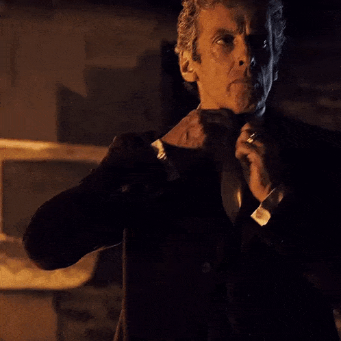 a man in a suit and tie is adjusting his tie in the dark