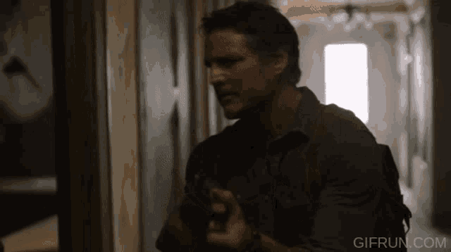 a man holding a gun in a hallway with gifrun.com written on the bottom right