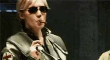 a woman wearing sunglasses is smoking a cigarette and blowing a kiss .