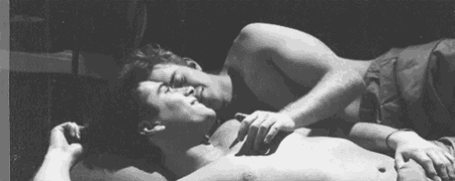 two men are laying on top of each other on a bed .
