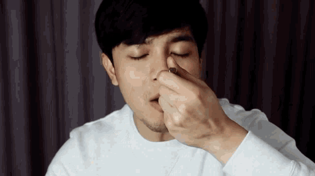 a man in a white shirt is cleaning his nose with his hands
